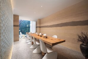 A modern dining room with a long wooden table, white chairs, and a view of trees through large windows. - Yunfuli Qingcheng Housi (Chengdu)