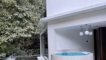 Un espacio exterior moderno con una piscina de hormigón, barandilla de cristal y zona de estar.