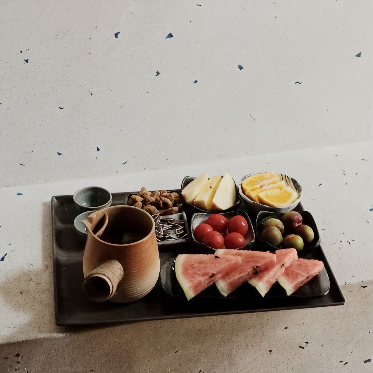 Bandeja con diversos alimentos, entre ellos frutas, frutos secos y una taza.