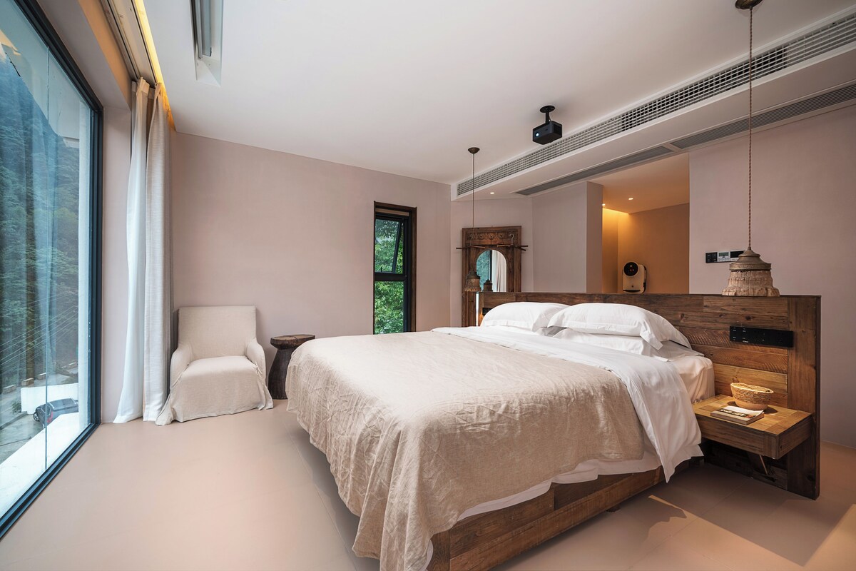 A modern bedroom with a large bed, a chair, a nightstand, and a large window.