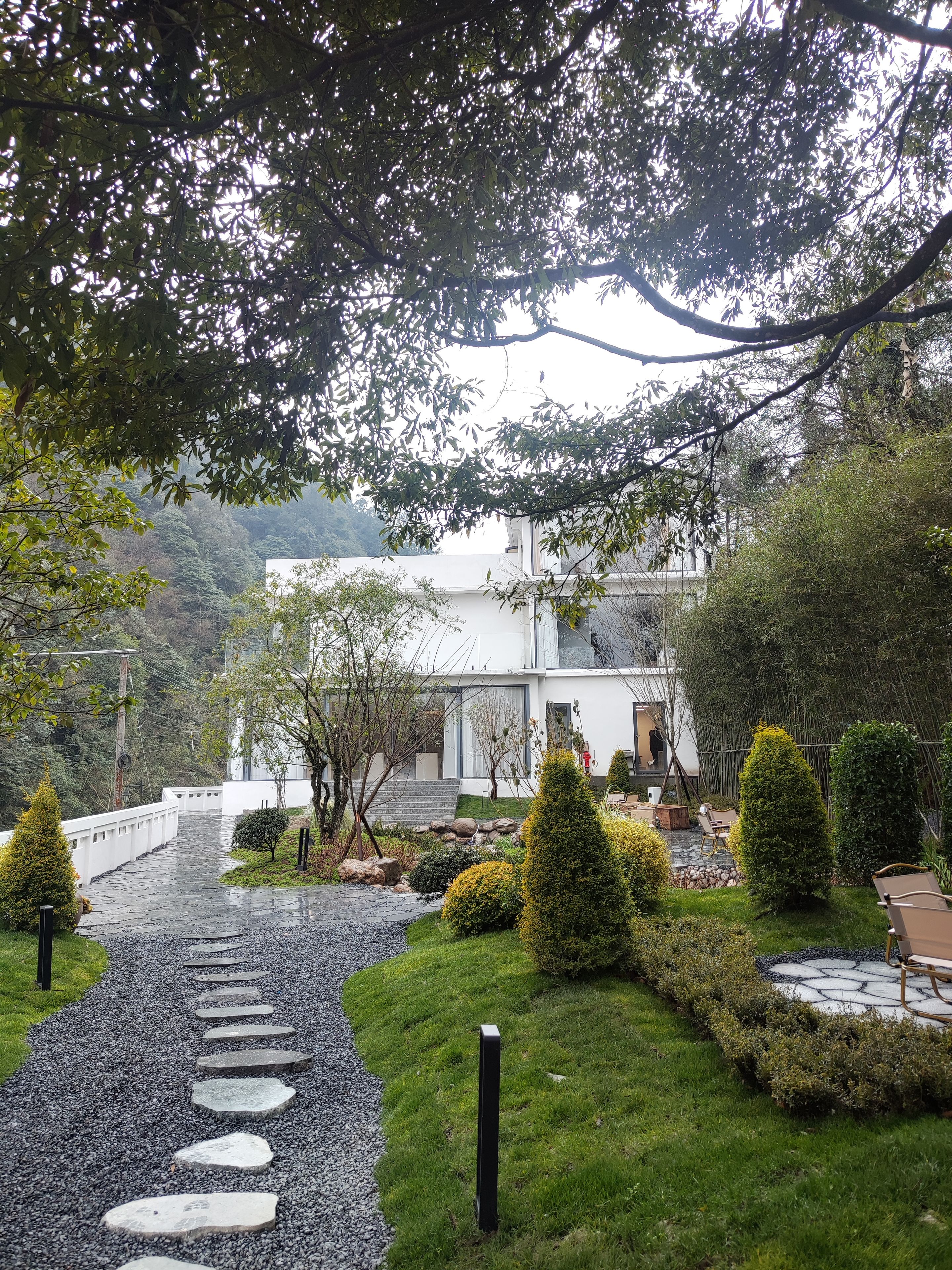 A pathway leading to a modern building surrounded by well-maintained greenery and a stone-tiled area.