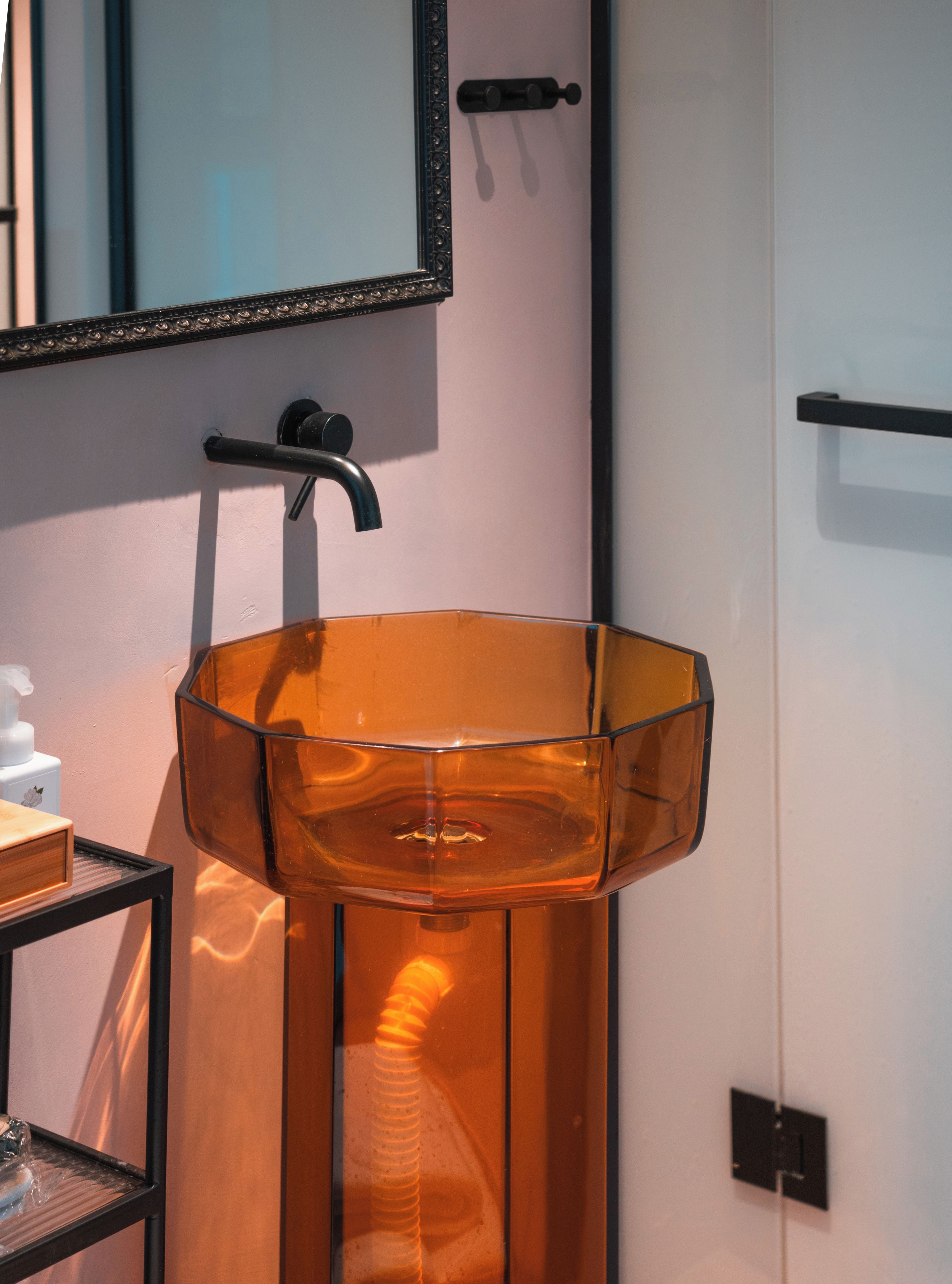 Un baño con un lavamanos de vidrio transparente, un espejo y un grifo negro.