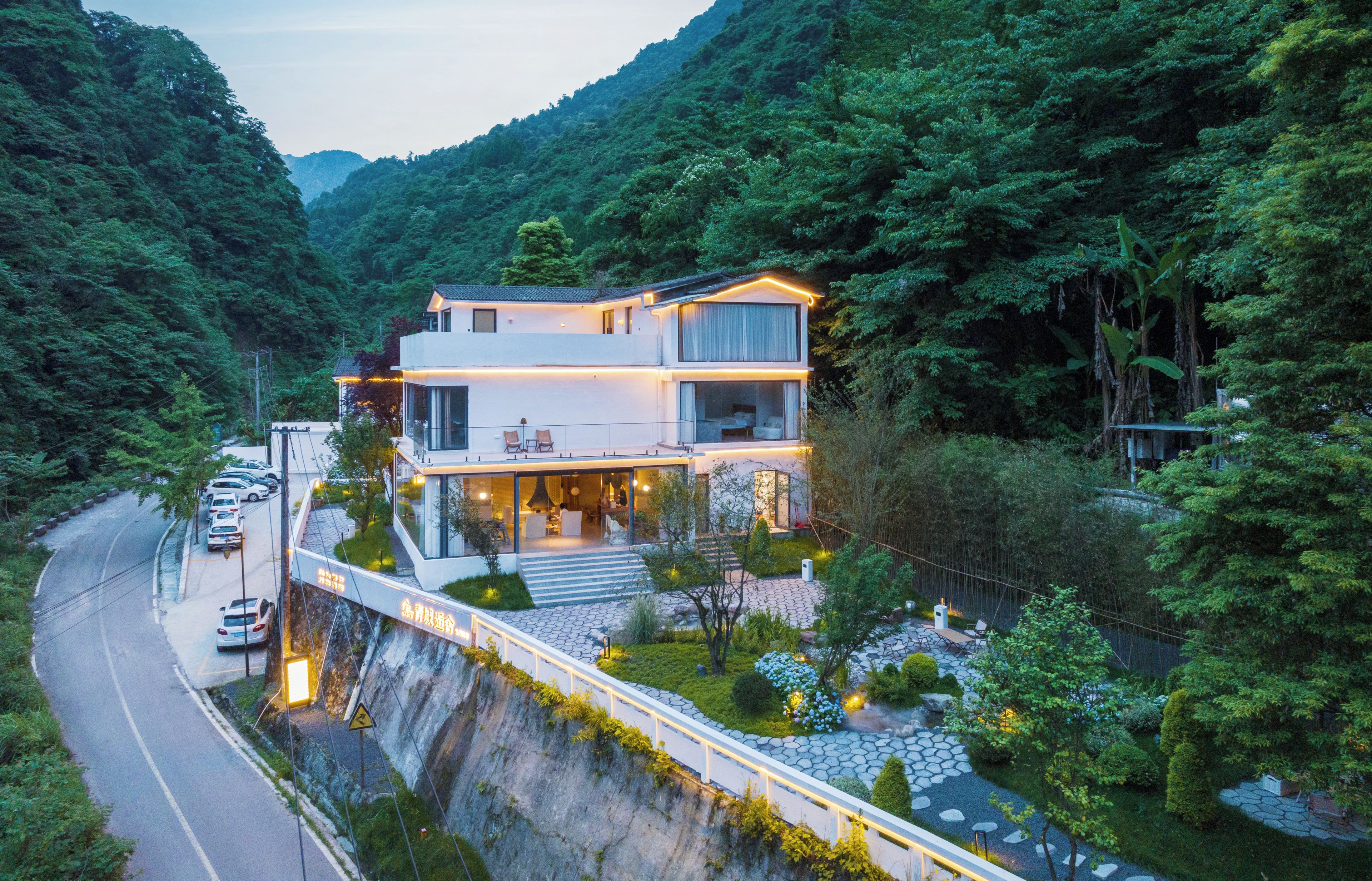 A modern two-story building with a glass facade, situated in a lush, mountainous area.
