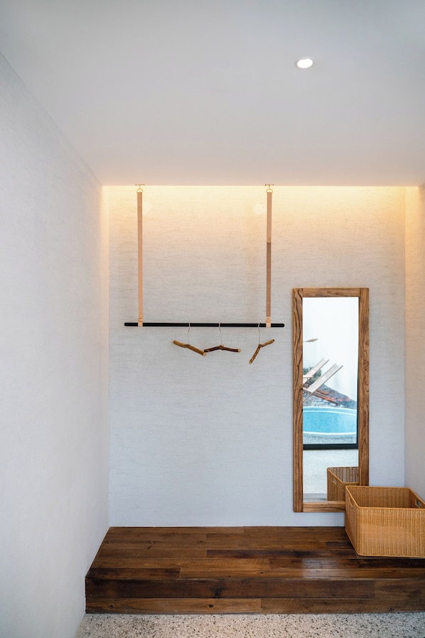 A room with a wooden floor, a white wall, and a mirror reflecting a pool.