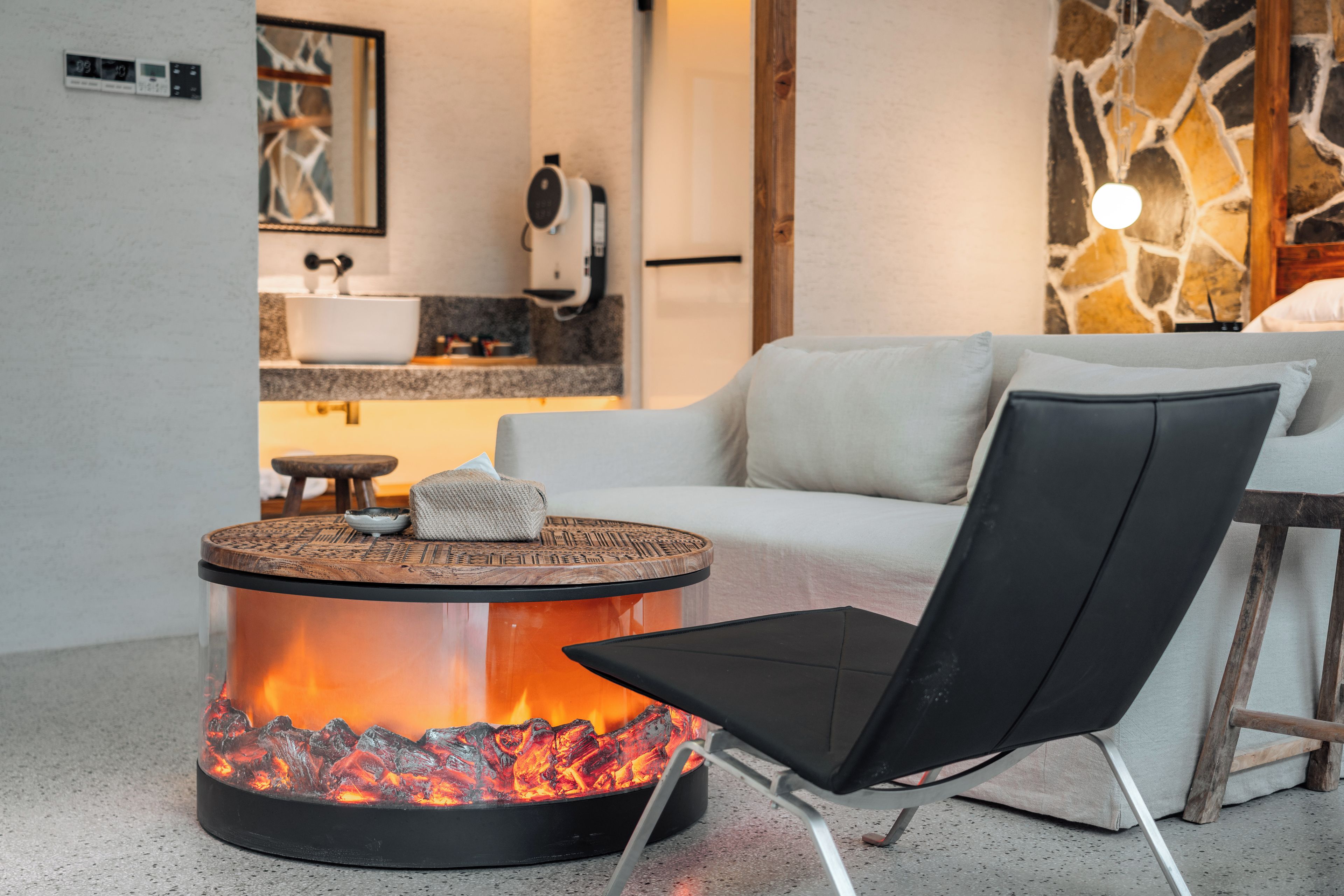 Una sala de estar moderna con una mesa de centro redonda que incorpora una chimenea, un sofá blanco y una silla negra.
