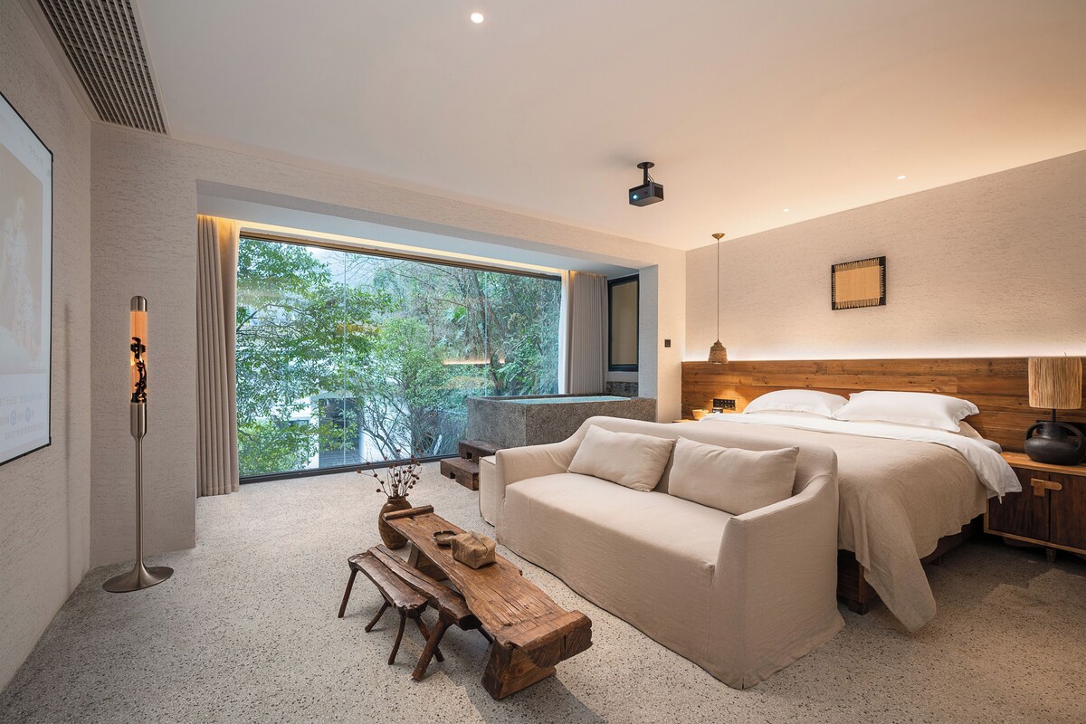 A modern bedroom with a large window, a bed, a sofa, and a wooden bench.