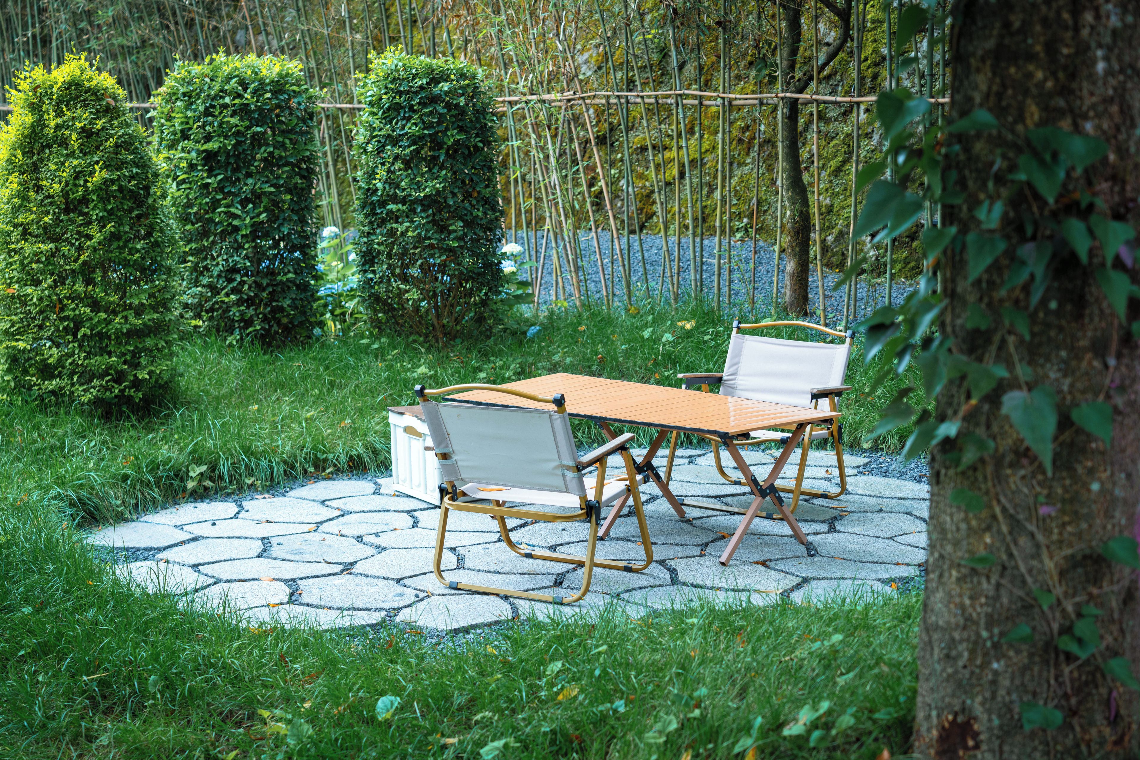A garden patio with a table and chairs, surrounded by greenery and a bamboo fence.