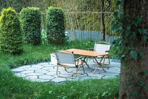 A garden patio with a table and chairs, surrounded by greenery and a bamboo fence.