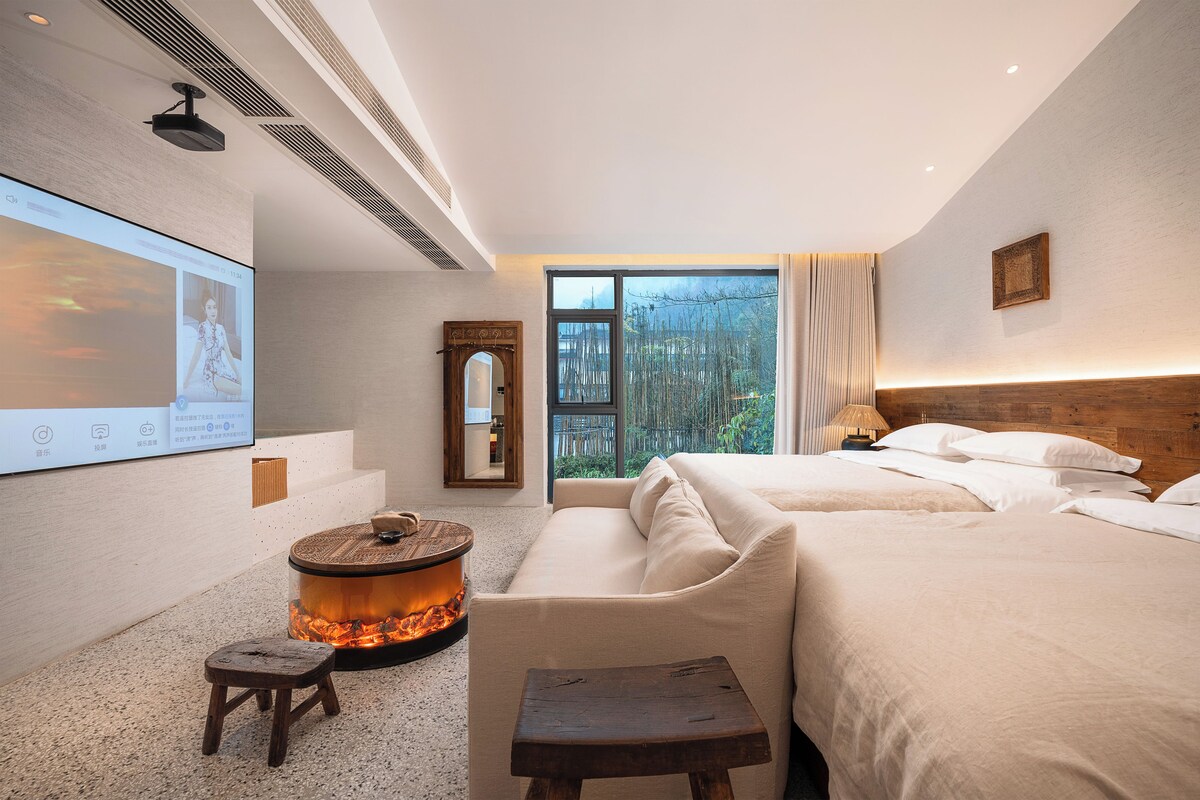 A modern hotel room with a large bed, a small seating area, a television, and a view of the outdoors.