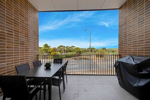 Un balcon avec une table et des chaises, un barbecue et une vue sur une route et la verdure.
