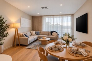 Un salon moderne avec un canapé, une table à manger pour quatre personnes, une lampe sur pied et une grande fenêtre avec des rideaux.