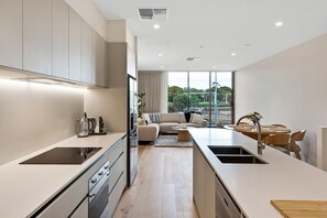 A modern kitchen with a central island, a dining area with a round table, and a living room with a sofa and curtains. - Spacious 3-Bed Townhouse In Mile End (Mile End)