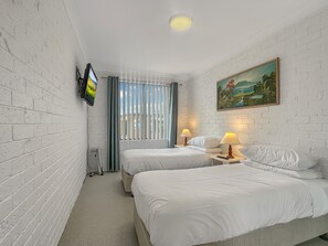 Een hotelkamer met twee bedden, een aan de muur bevestigde televisie, een schilderij en een raam met jaloezieën.