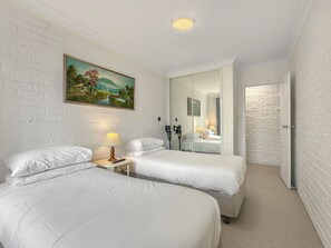 Ein Hotelzimmer mit zwei Betten, einem Bild an der Wand, einem Spiegel und einer Tür zu einem anderen Raum.