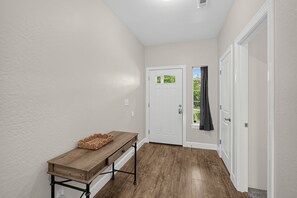 A hallway with a wooden bench, a white door, and a window with a view of greenery. - Medford Home Near Wineries | Fenced Yard, Pets OK (Medford)