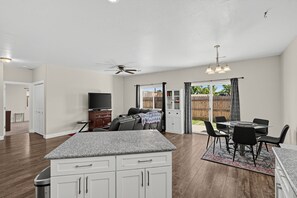 A spacious kitchen with a granite countertop, a dining area with a table and chairs, a ceiling fan, and a view of the backyard through a sliding glass door. - Medford Home Near Wineries | Fenced Yard, Pets OK (Medford)