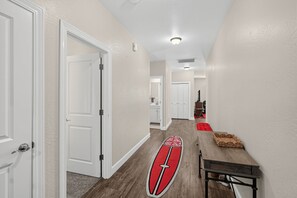 Un pasillo con puertas blancas, piso de madera y un tapete con forma de tabla de surf roja.
