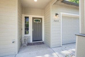 Ein Haus mit einer grauen Haustür, einer kleinen Veranda mit einem weißen Metalltisch und einer Garage mit der Nummer 2642.