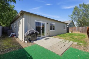 Ein eingeschossiges Haus mit überdachter Grillgelegenheit, Terrasse und umzäunter Garten.