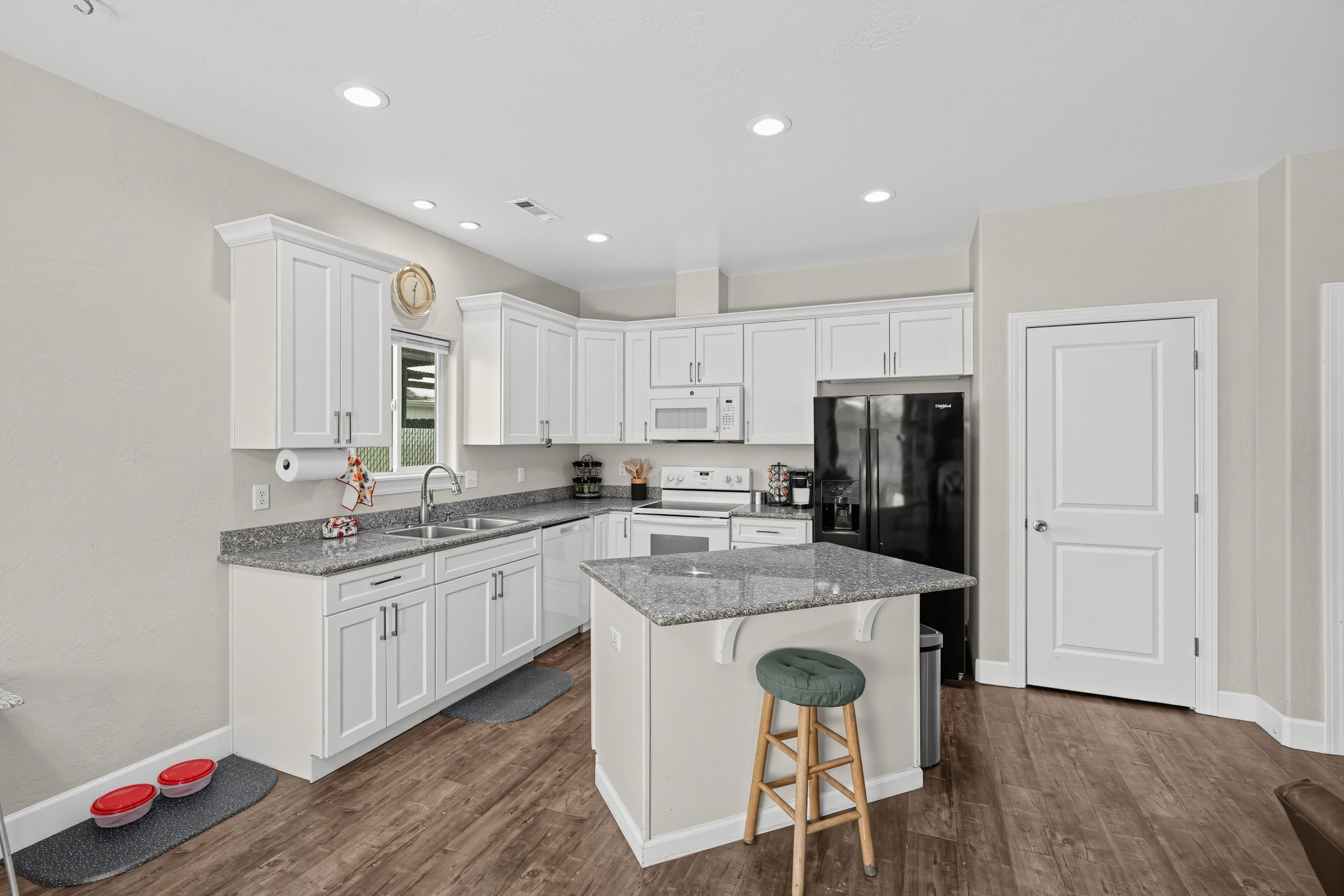 A modern kitchen with white cabinetry, granite countertops, a stainless steel refrigerator, and a wooden stool.
