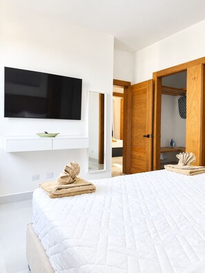 Ein Schlafzimmer mit einem großen Bett, einem flachbildfernseher an der Wand, einem Spiegel und Holztüren zu einem weiteren Raum.