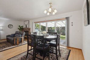 Ein modernes Wohnzimmer mit Kamin, einer Essecke mit rundem Tisch und Stühlen sowie einem großen Fenster mit Blick ins Freie.