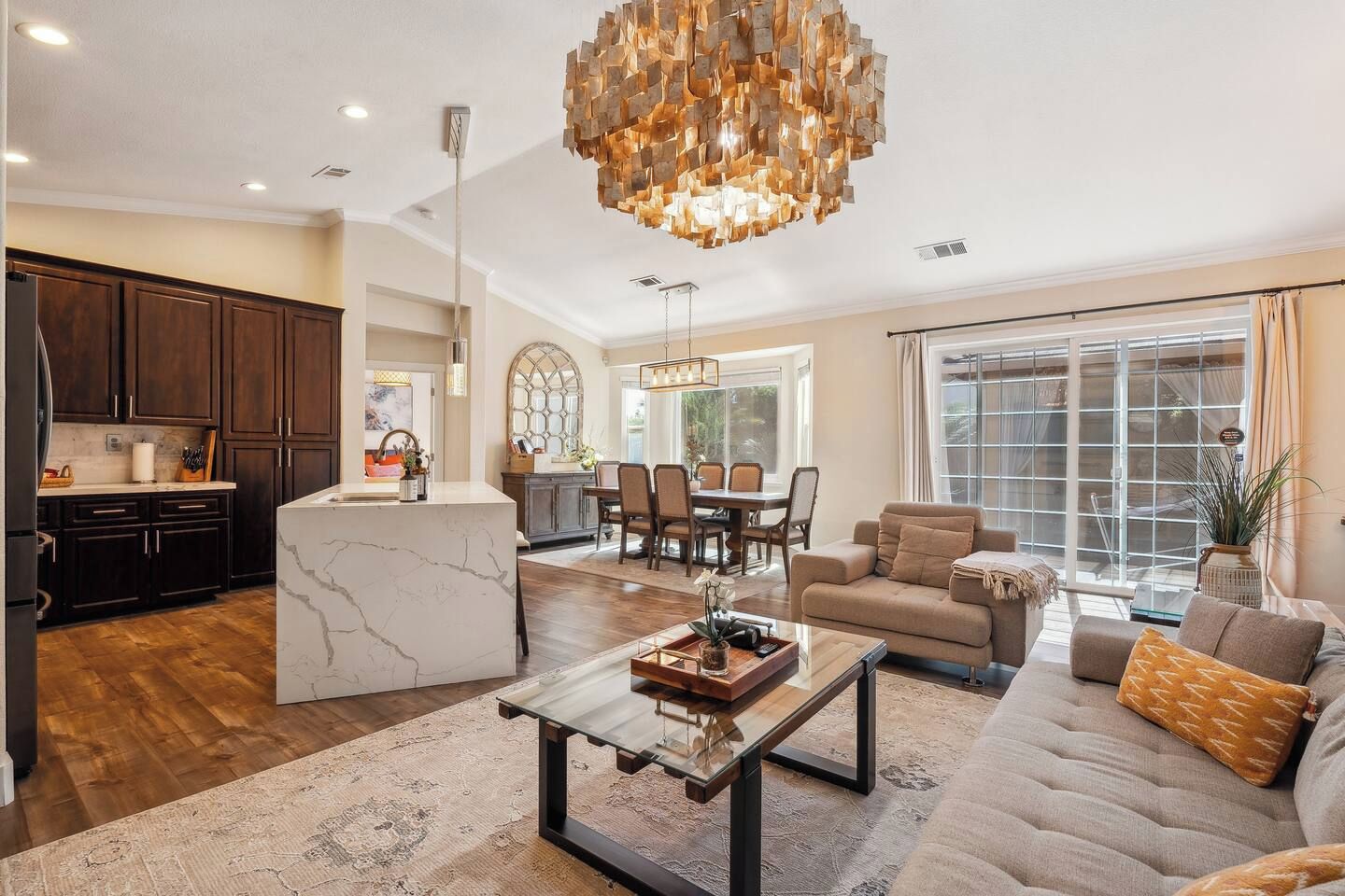 A spacious living area with a marble island, a dining area with a chandelier, and a large window with curtains.
