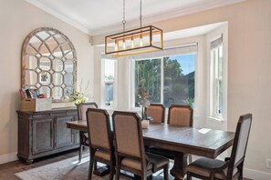Une salle à manger avec une table en bois, six chaises, un lustre et un grand miroir au-dessus de la table.