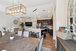 A modern kitchen with dark cabinetry, a central island, and a dining area with a wooden table and chairs. - Spacious 4BR/2BA Roseville Oasis w/ Pool & Lounge (Roseville)