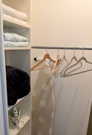 A closet with shelves holding folded towels and a hanging rack with hangers.