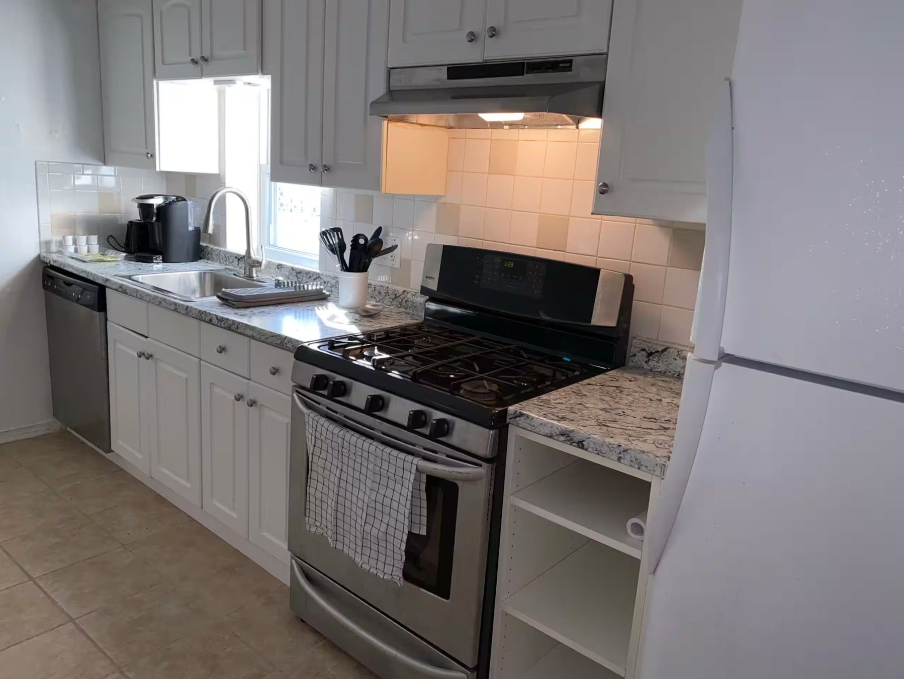 A kitchen with white cabinets, a stainless steel stove, a dishwasher, and a window above the sink.
