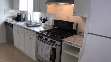 A kitchen with white cabinets, a stainless steel stove, a dishwasher, and a window above the sink.