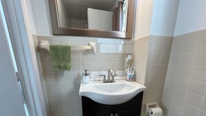 Ein Badezimmer mit einem weißen Waschbecken, einem Spiegel, einem Handtuchhalter mit einem grünen Handtuch, einer Mülleimer und einem Toilettenpapierhalter.
