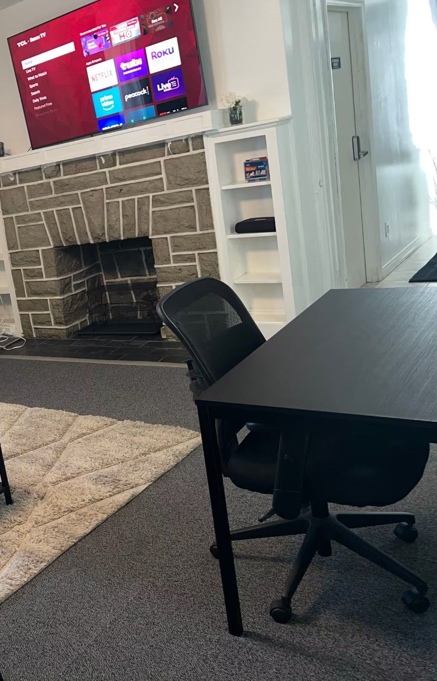 A conference room with a stone fireplace, a flat-screen TV mounted above it, and a table with office chairs.