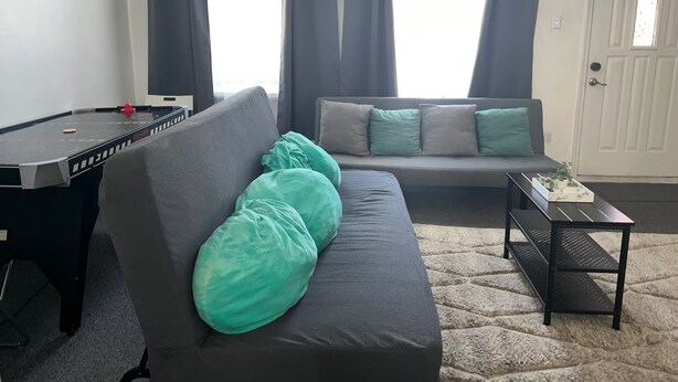 Ein Wohnzimmer mit Billardtisch, einer Couch mit Kissen, einem kleinen Tisch mit einer Pflanze und einer Tür.