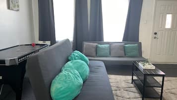 A living room with a pool table, a sofa with cushions, a small table with a plant, and a door.
