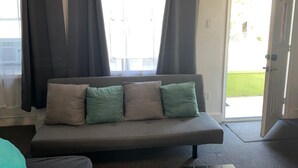 Ein Zimmer mit einem grauen Sofa, zwei grünen Kissen und einer zur Außenseite führenden Tür.