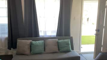 Una stanza con un divano grigio, due cuscini verdi e una porta che dà sull'esterno.
