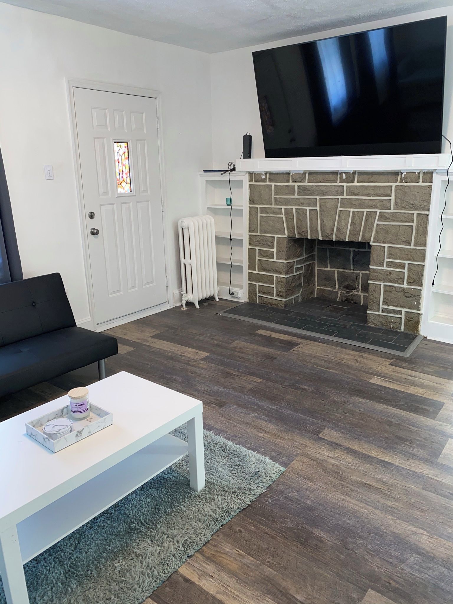 A living room with a fireplace, a television mounted above it, a white door with a stained glass window, and a black sofa.