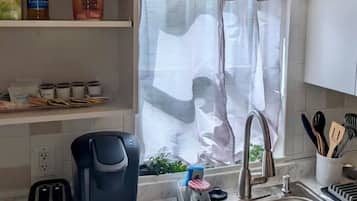 Una cucina con lavello in acciaio inossidabile, macchina del caffè e finestra con tenda.