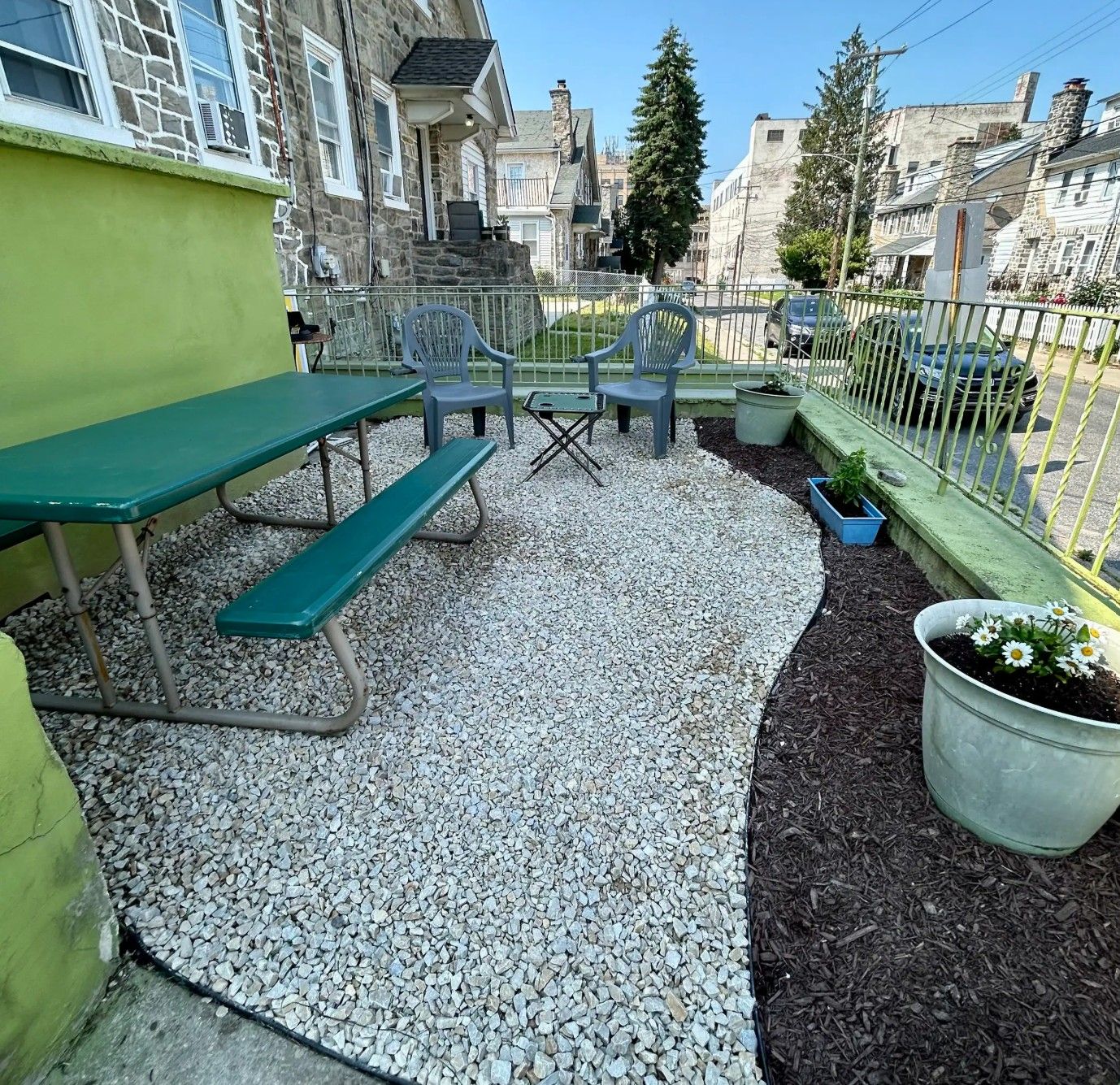 An outdoor patio with a table and chairs, surrounded by a gravel area and a metal fence.