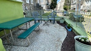 Eine Terrasse im Freien mit Tisch und Stühlen, umgeben von Kiesflächen und einem Metallzaun.