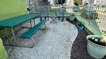An outdoor patio with a table and chairs, surrounded by a gravel area and a metal fence.