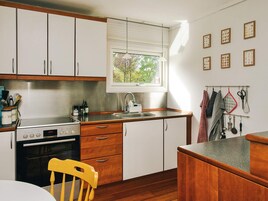 Una cocina con armarios blancos, estufa, pileta y ventana con persianas.