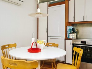 A compact kitchen with a round dining table, wooden chairs, a refrigerator, a stove, and a hanging light fixture. - 4 Person Holiday Home in Hojby (Hojby)