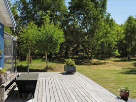 Una terraza de madera con una mesa y sillas, rodeada de follaje y árboles.