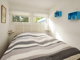 Un dormitorio con cama, una ventana con persianas, una mesita de noche y dos estantes azules en la pared.