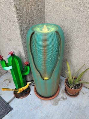 Una jardinera grande y texturizada con una fuente central, un cactus verde y una planta de aloe.
