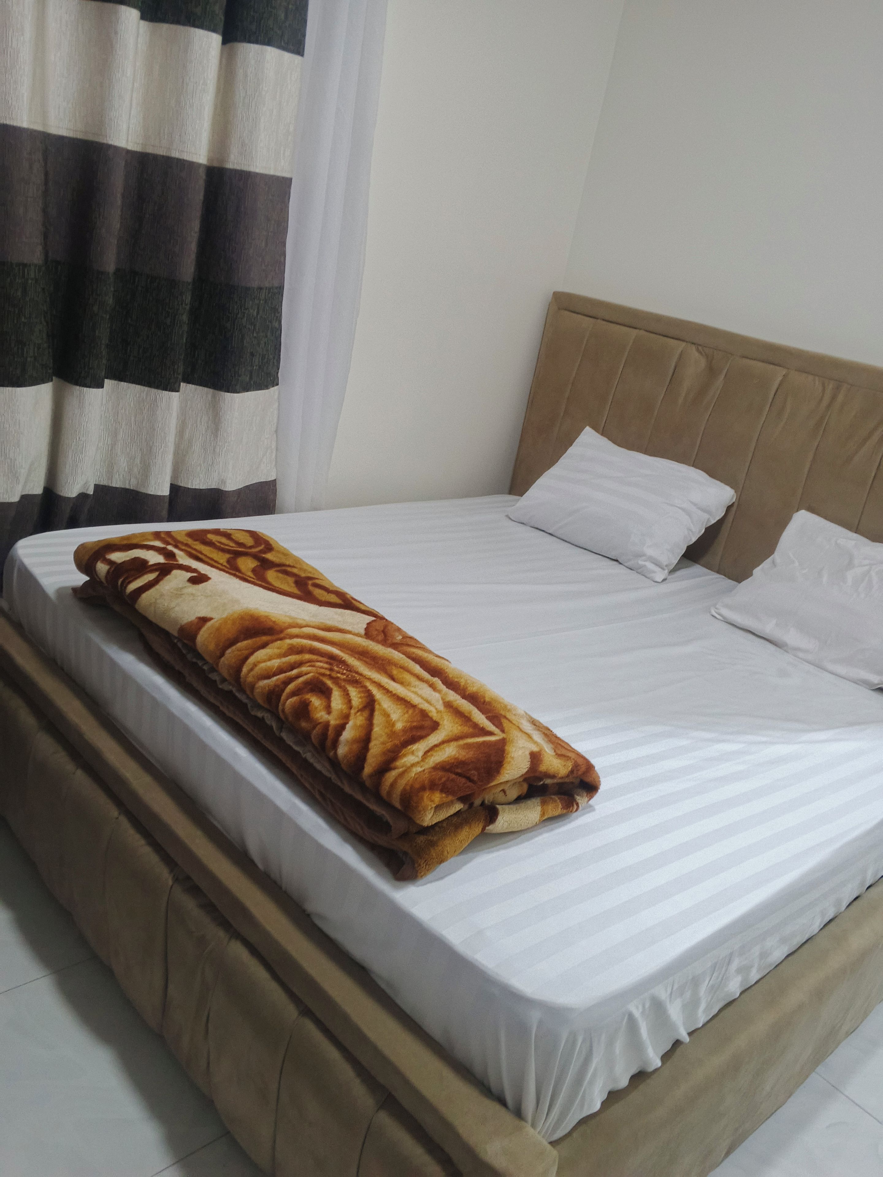 Un lit avec un matelas blanc, une tête de lit beige et une couverture marron.