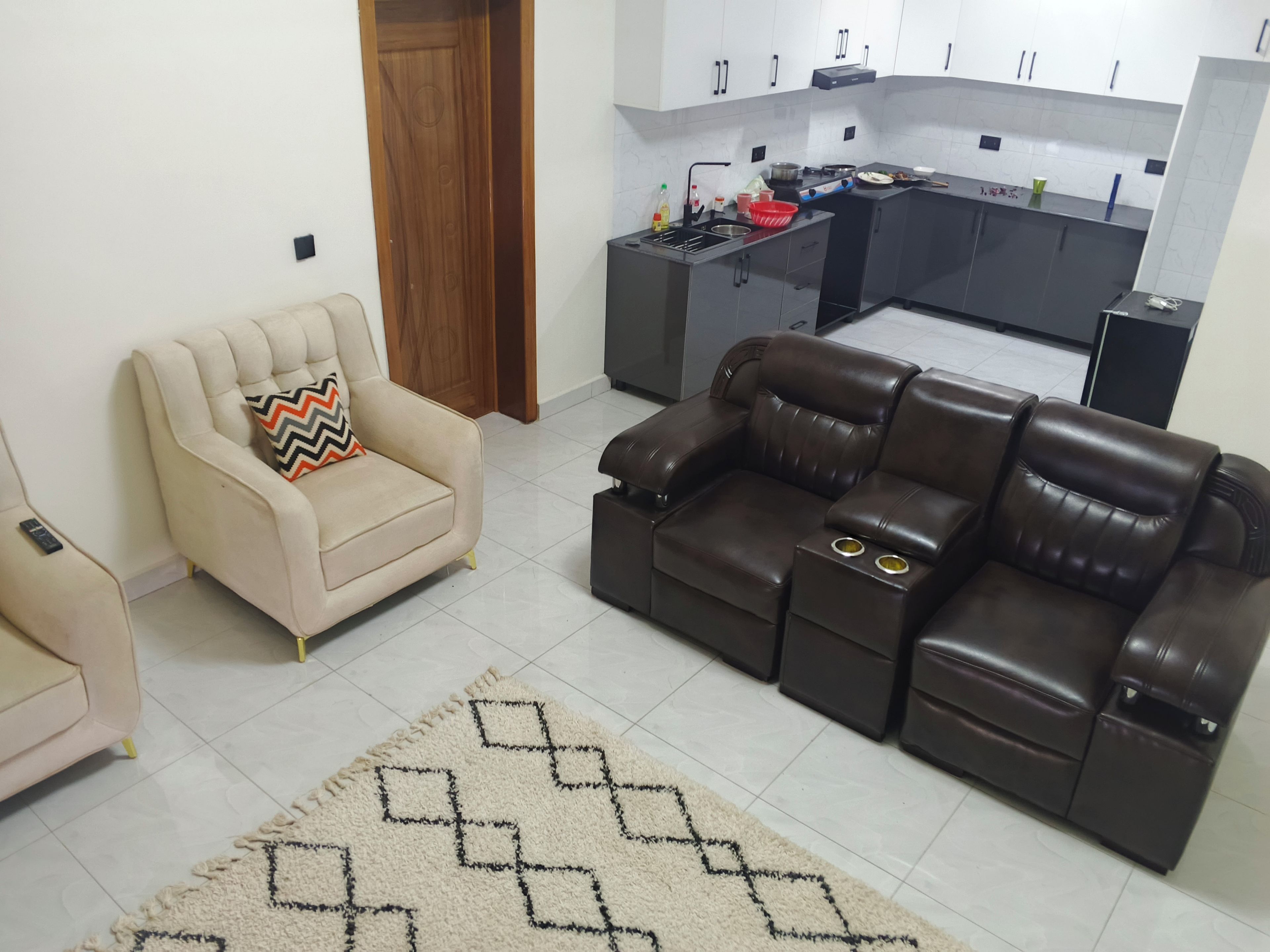 Un salon avec un canapé beige, un canapé en cuir marron et un tapis à motifs.